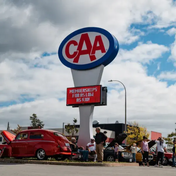 Copilot said:  Image 1 Alt Text:  CAA Atlantic roadside sign overlooking a car show, with classic vehicles on display and event attendees gathered around the parking lot outside the Dartmouth branch