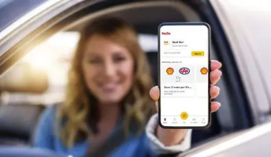 A person seated in a car extends a smartphone toward the camera, showing a rewards app screen with loyalty offers and account information.