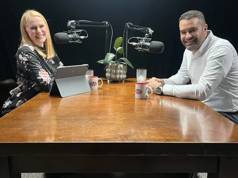 Julia and Danny sitting together at a table doing a podcast about roadside realities